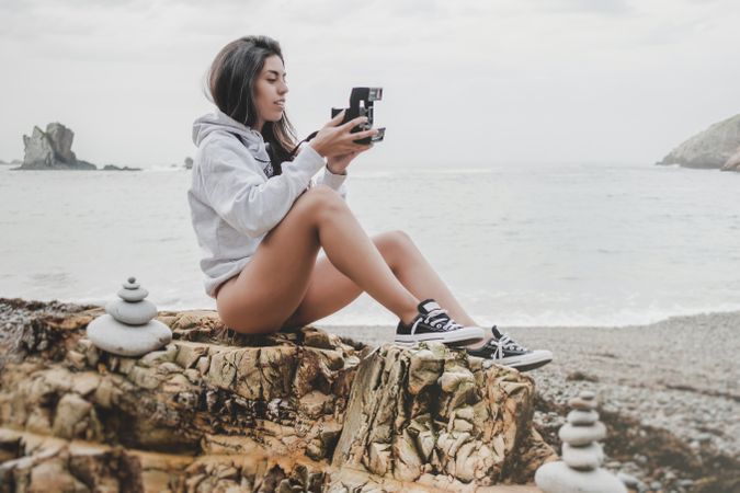 Woman with camera on shore near stones and water