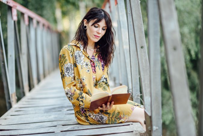 Calm female sitting on a rural bridge enjoying reading
