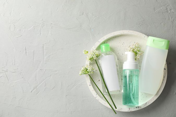 Liquids for body care in different bottles and allium flowers on plain background