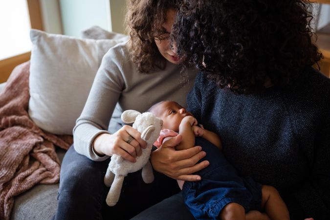 Two women consoling their baby with a toy on the couch