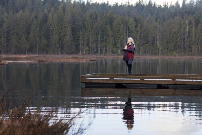 Woman in meditative prayer pose on dock over lake
