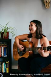 Young woman playing guitar laughing and looking away from camera bGRzv4