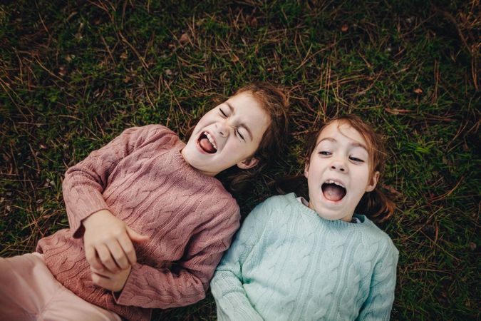 Top view of two little girls lying on green grass and laughing