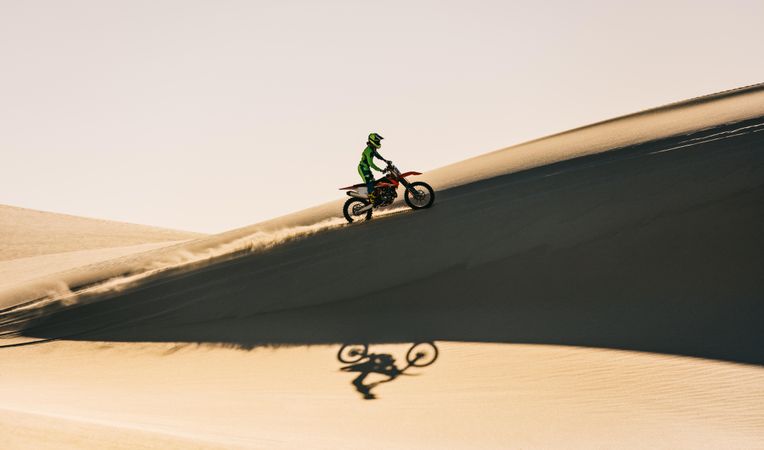 Side view of motocross rider going up over sand dunes