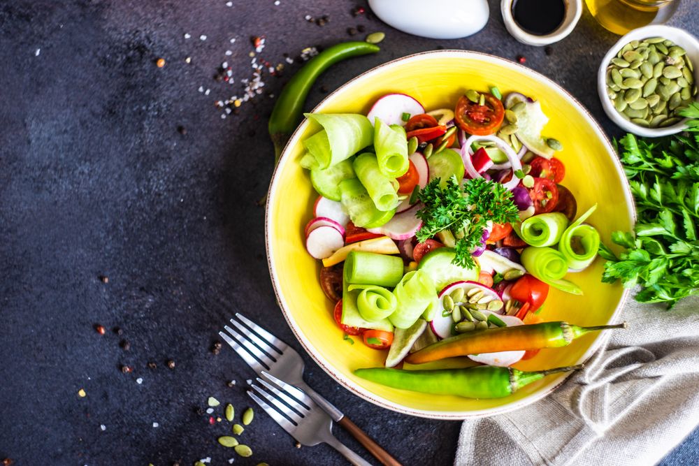 Top view of healthy raw salad with freshly chopped vegetables served with nuts and garnish