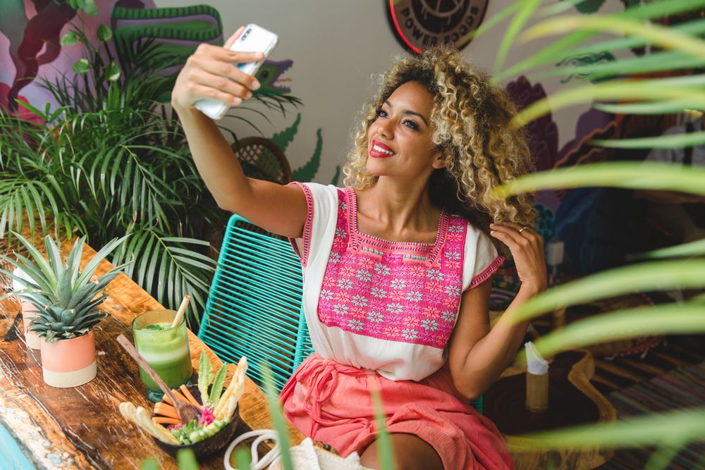 Black female with fresh shake taking selfie on smartphone