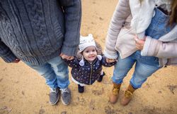 Happy girl looking up while holding her parents hand outside
