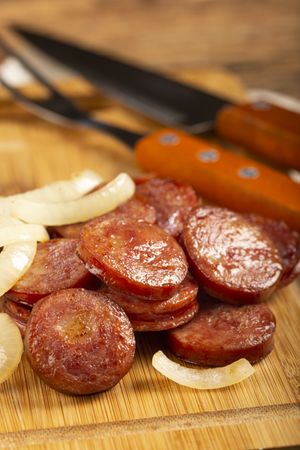 Sliced calabrese sausage with onion on wooden background.