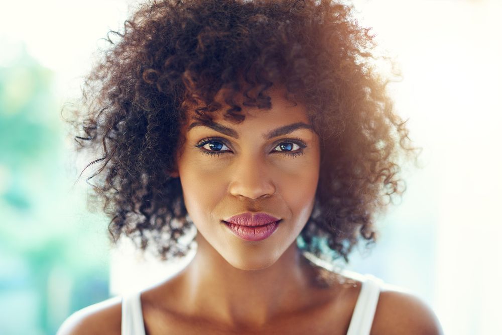 Female with curly hair looking at camera on blurry leafy background