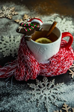 Cup of mulled tea wrapped in cosy scarf with cute gingerbread cookie
