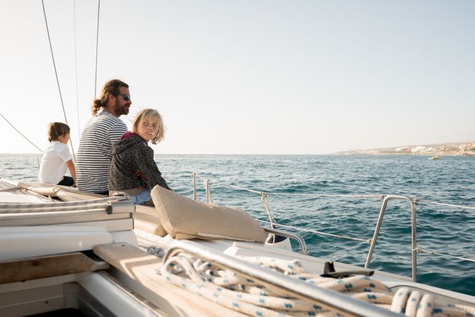 Man with children sitting on edge of yacht in sea