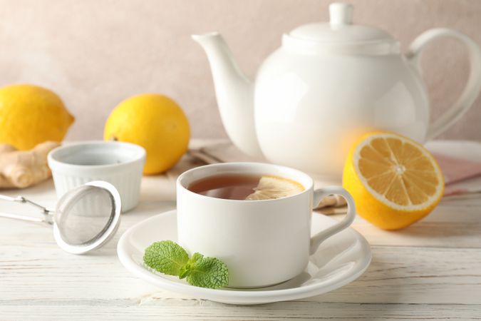 Cup of tea with lemon, mint, strainer, ginger and teapot on wooden background, space for text