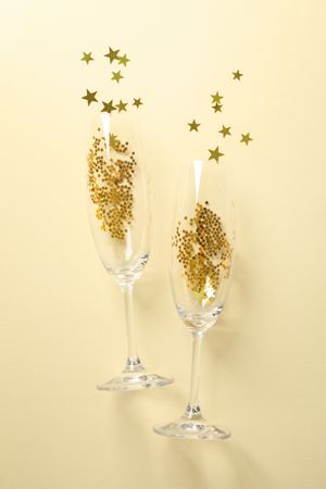 Champagne glasses with glitter on beige background, space for text