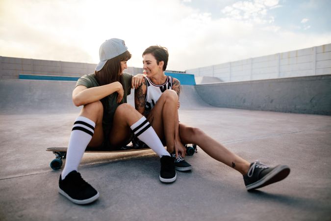 Woman skateboarders sitting on long board and looking at each other