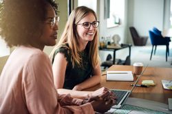 Two happy female colleagues smiling while listening during a meeting