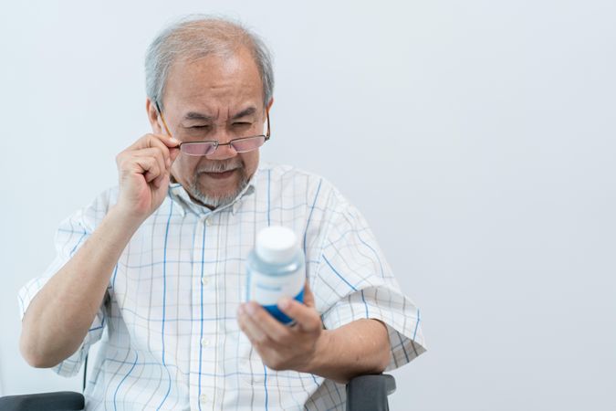 Mature male pulling down glasses to read label on bottle