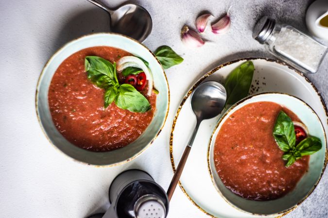 Top view of two bowls of traditional gazpacho soup with olive oil, salt, basil, garlic and pepper