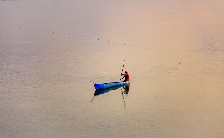 Man in blue kayak on sea during sunset