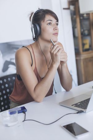 Woman sitting at desk with headphones and thinking out problem