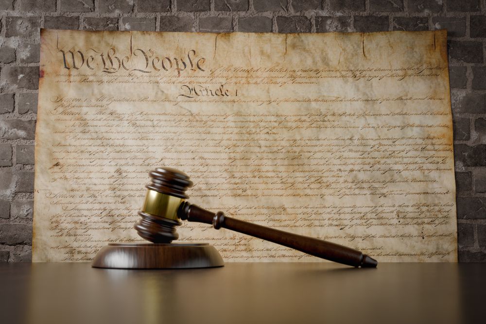 United States Constitution On Wall with Gavel Resting on Table in Front.