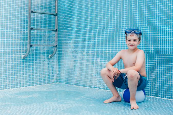 Boy sitting on ball in empty pool