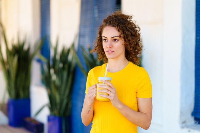Contemplative woman in yellow dress sipping similar colored smoothie