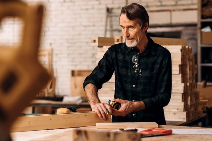 Older male carpenter measuring a piece of wood