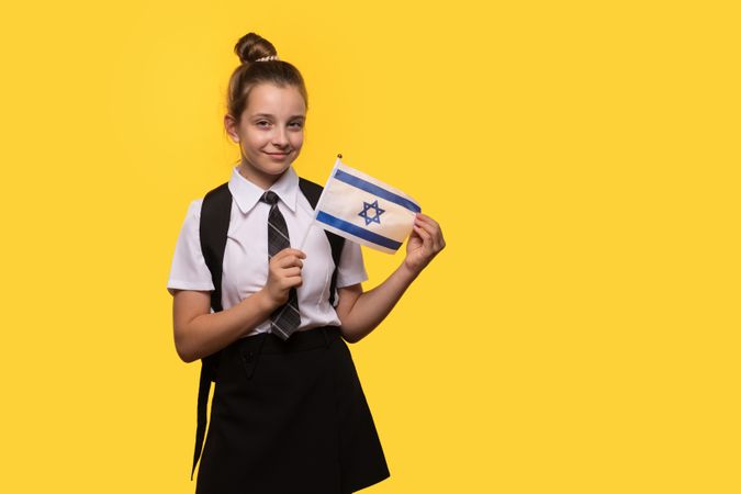 Schoolgirl proudly holds Israeli flag while smiling.