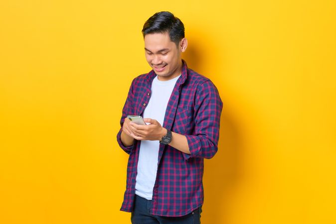 Happy Asian man in plaid shirt  looking down at smartphone