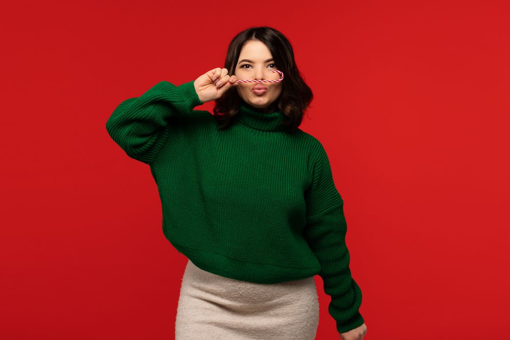 Woman in green sweater holding candy cane like mustache