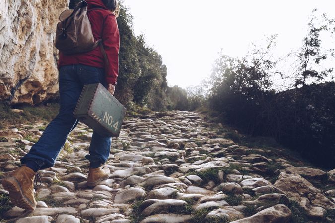 Woman with case walking on rocks above stream