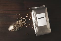 Bag of coffee beans with whole beans spilling out of small glass