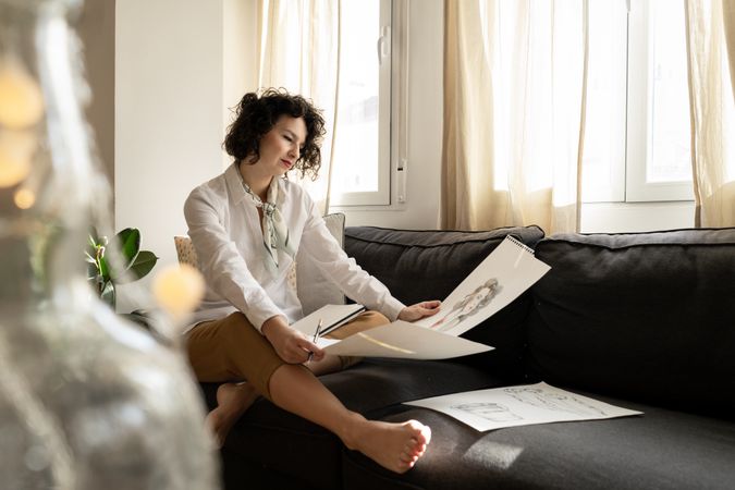 Woman drawing on papers on sofa in room