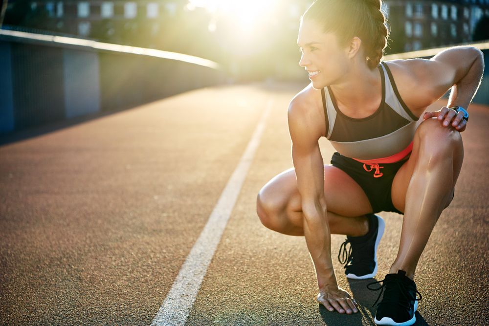 Muscular woman crouching down on sunny bridge
