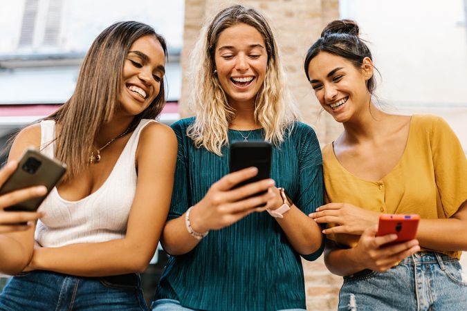 Smiling multi-ethnic female friends having fun together using mobile phone