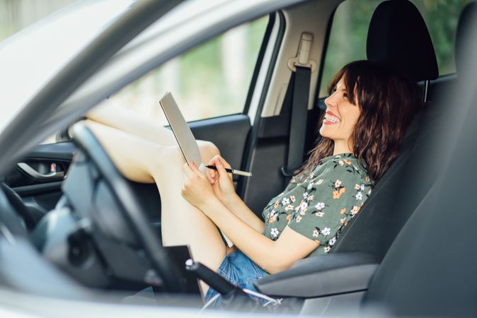 Happy female wearing flowered shirt and shorts sitting in parked car