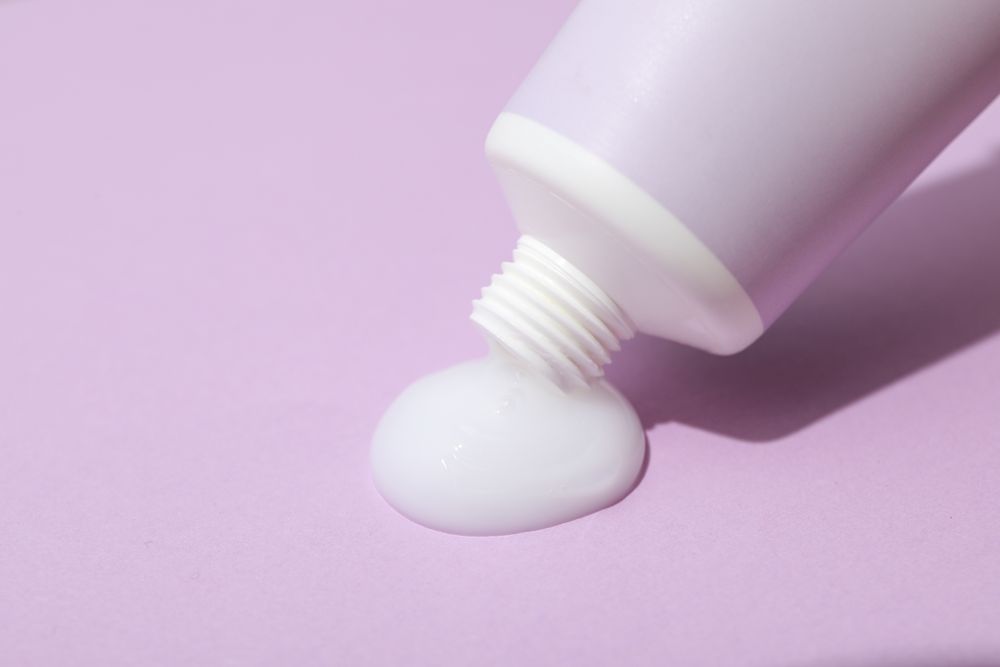 Tube with cream on purple background, close up