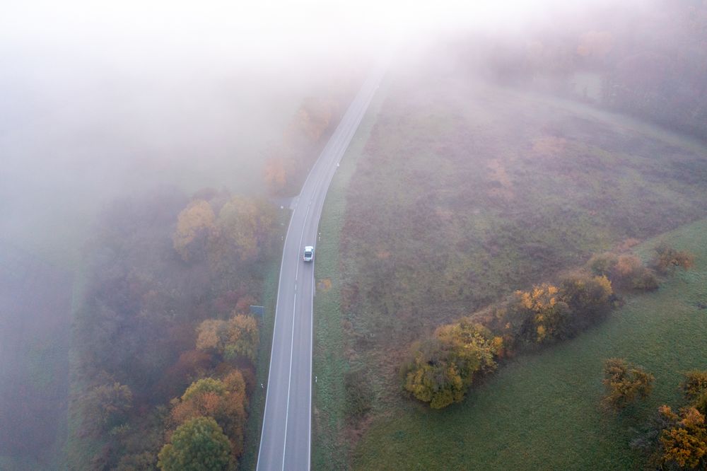 Drone aerial image with a winding road crossing an autumn forest on a foggy morning