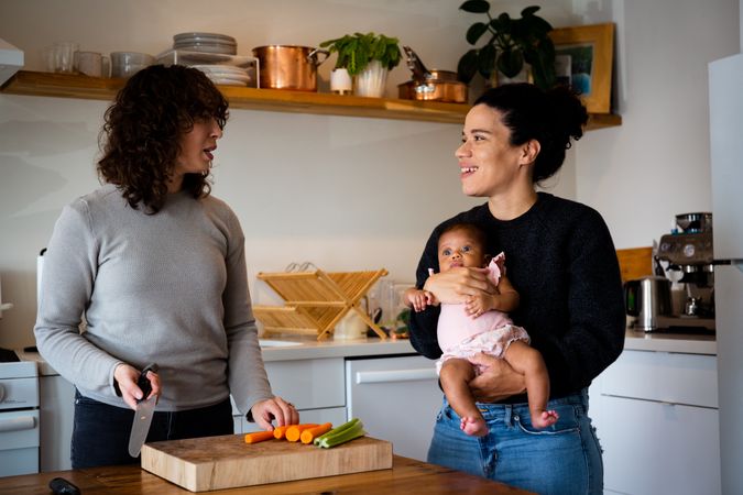 One woman prepping vegetables with other holding baby