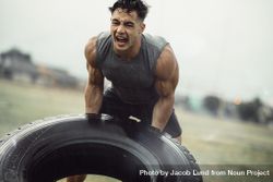 Tough young male athlete doing a tire flip exercise in the rain bGxJa0