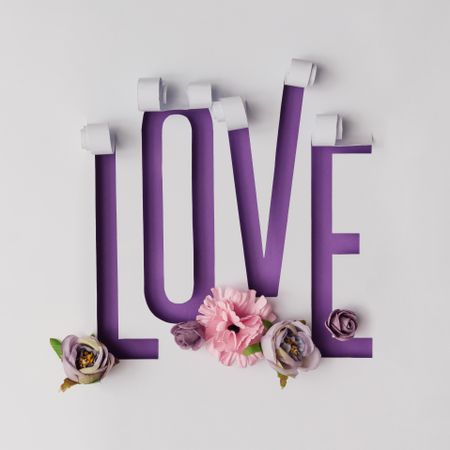 Word LOVE made of torn paper on violet background with flowers