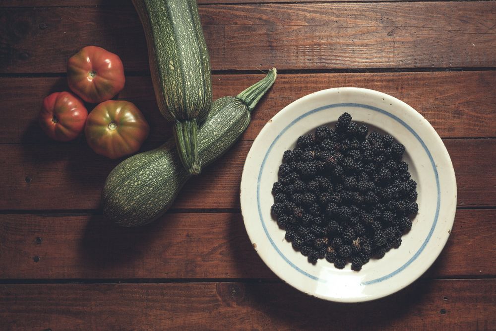 Ripe blackberries garnished by vegetables in bowl on wooden background