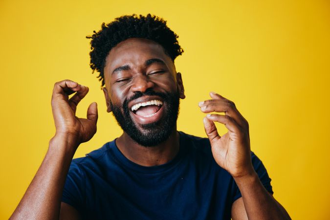 Portrait of ecstatic Black man with both hands to his head on yellow background