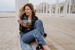 Content woman eating salad from plastic bowl sitting on wooden terrace