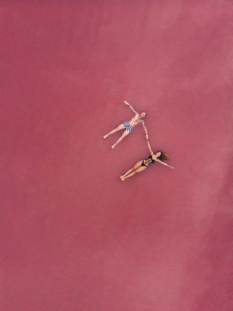 Idyllic couple in swimwear floating in pink water of lake