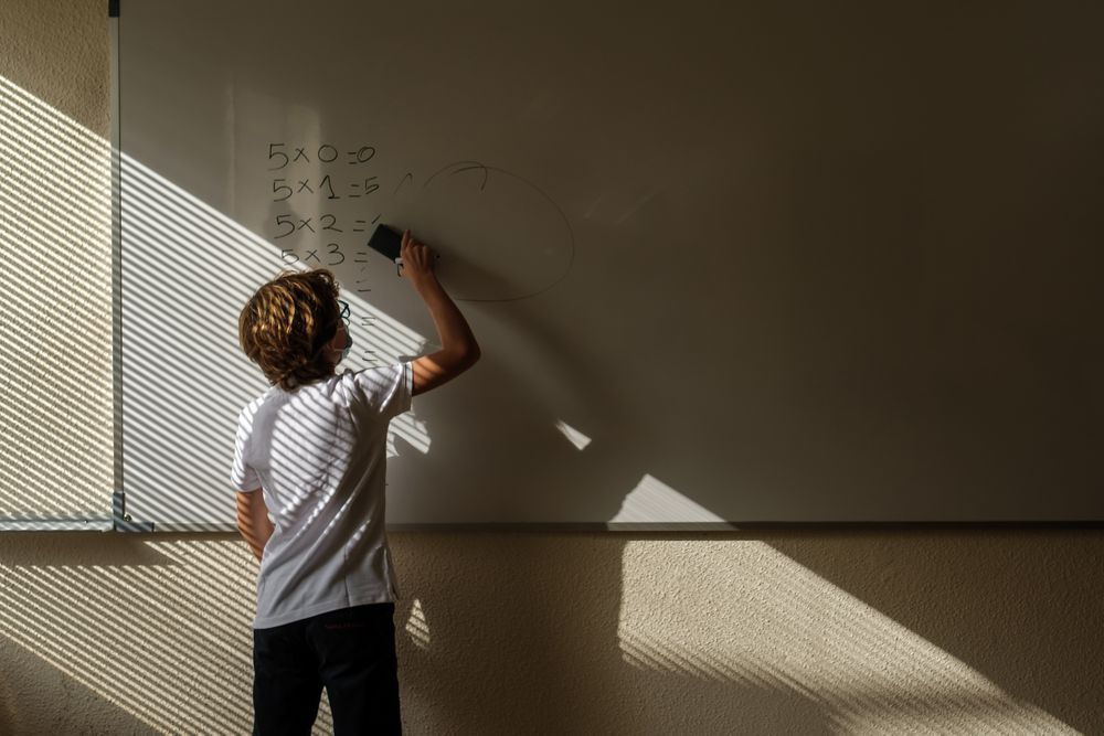 Unrecognizable schoolchild erasing math example from whiteboard