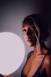 Black adult woman with illuminated balloon in darkness looking at camera