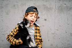 Kid holding dog and yawning against concrete wall