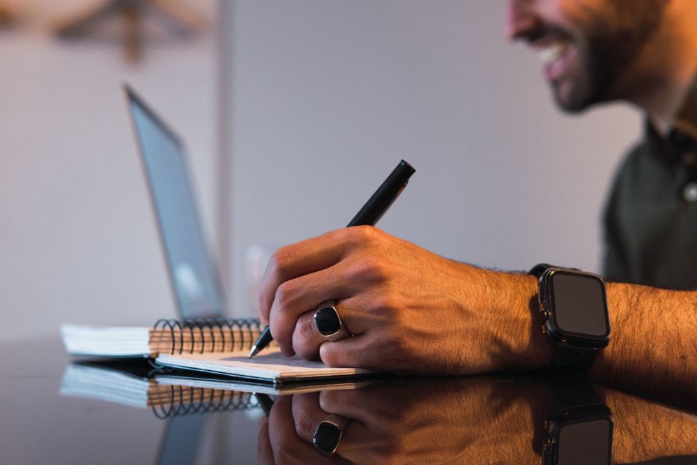 Anonymous man writing in notebook near laptop