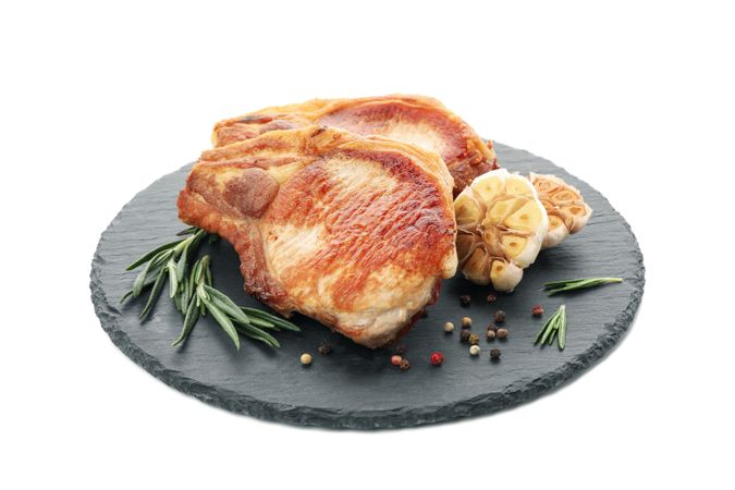 Tray with fried pork steaks isolated on light background. Grilled food